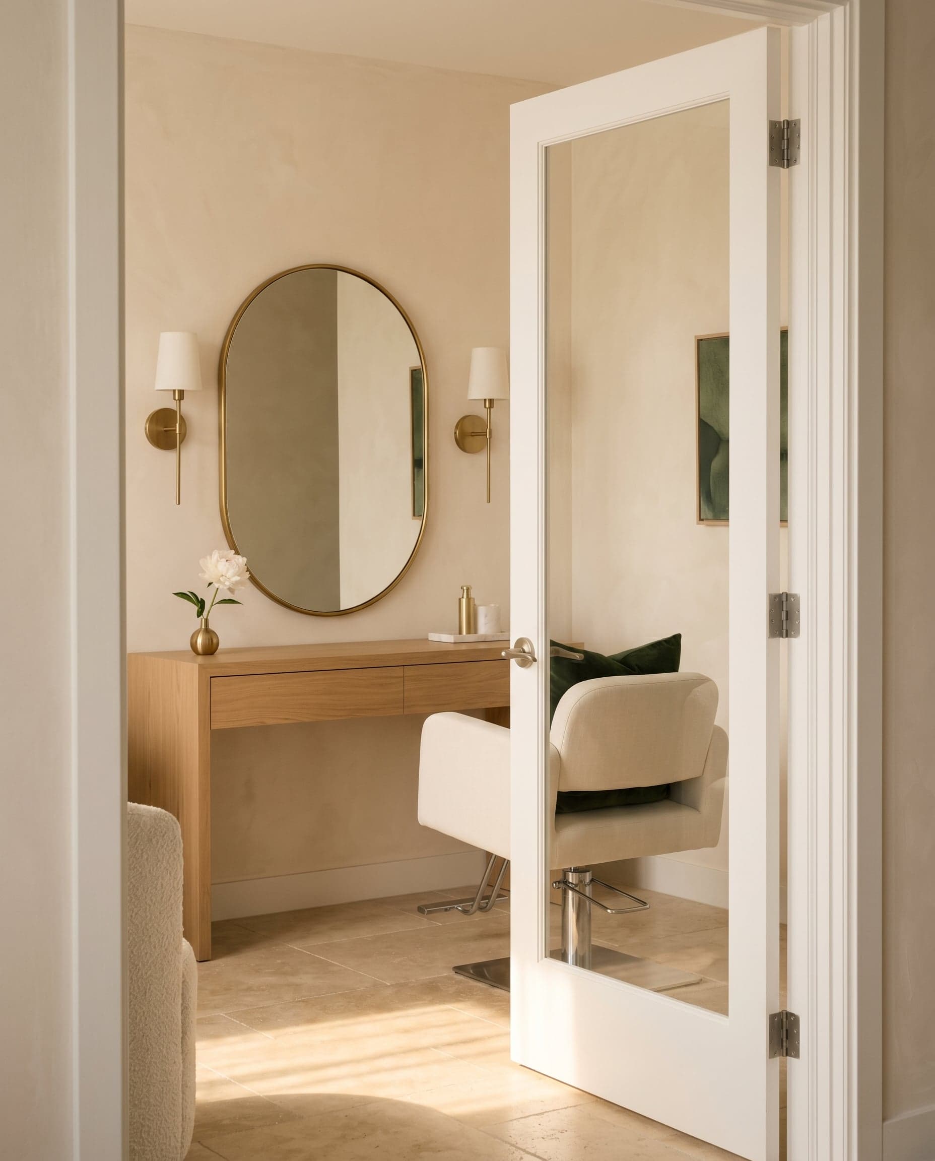 Cream-walled private salon suite with brass sconces and an oak vanity in golden afternoon light.